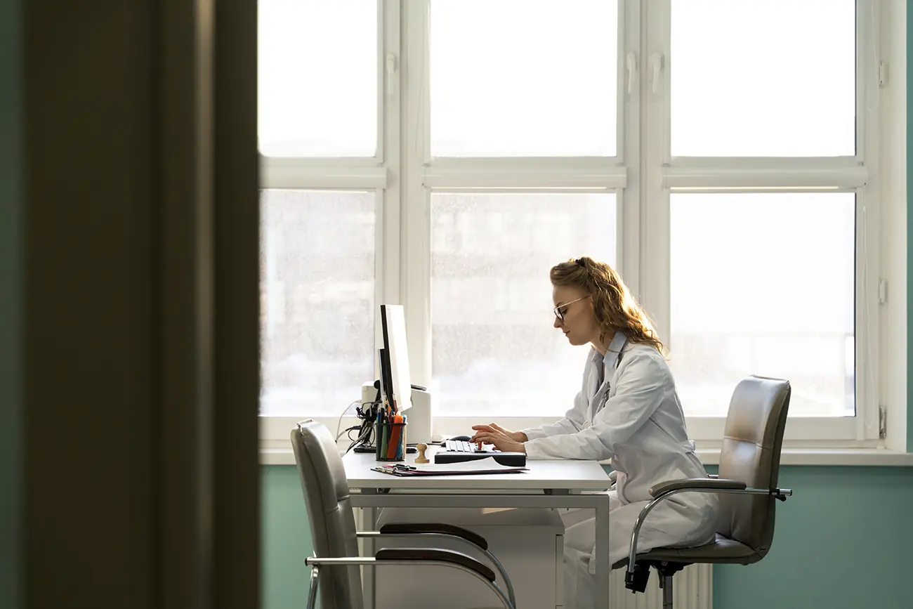 Médica concentrada trabalhando em um computador em um consultório moderno, ilustrando como o coworking médico otimiza custos operacionais para profissionais de saúde.
